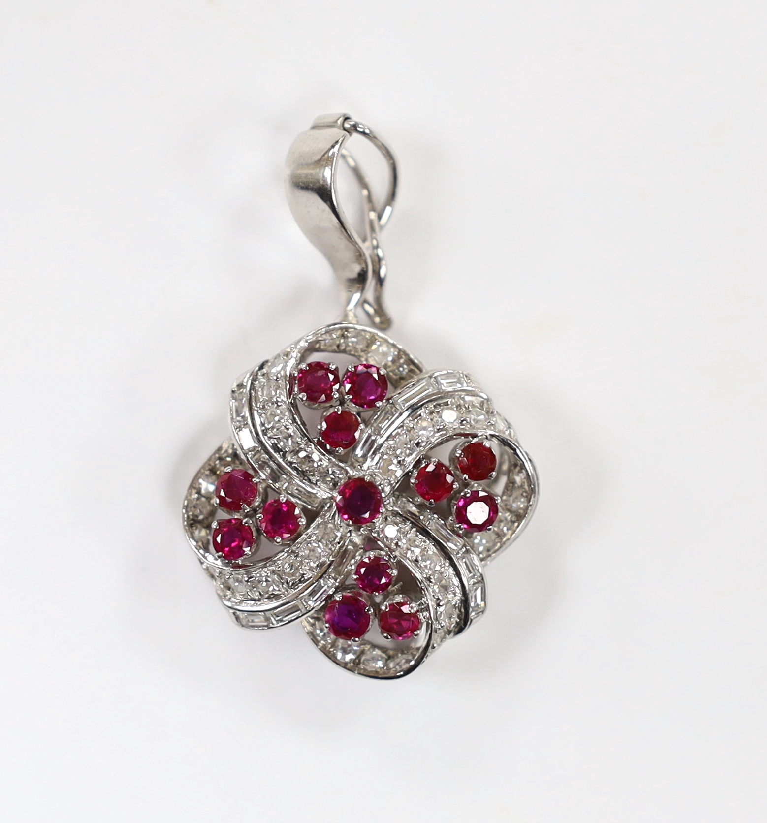 A modern 14k white metal, ruby and diamond cluster set scroll pendant, 25mm, gross weight 11 grams.